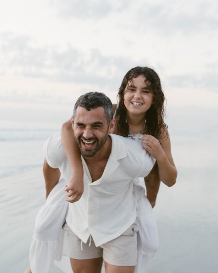 Andreas giving his daughter a piggyback on the beach, both laughing